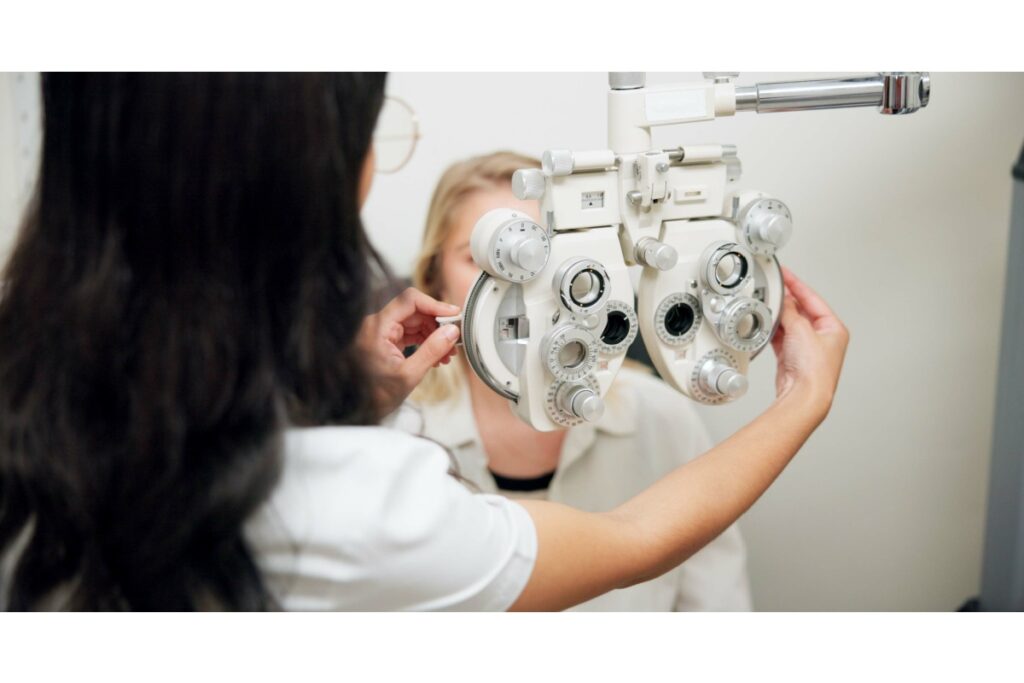 An optometrist adjusting a phoropter while a patient sits behind the device during a comprehensive eye exam.