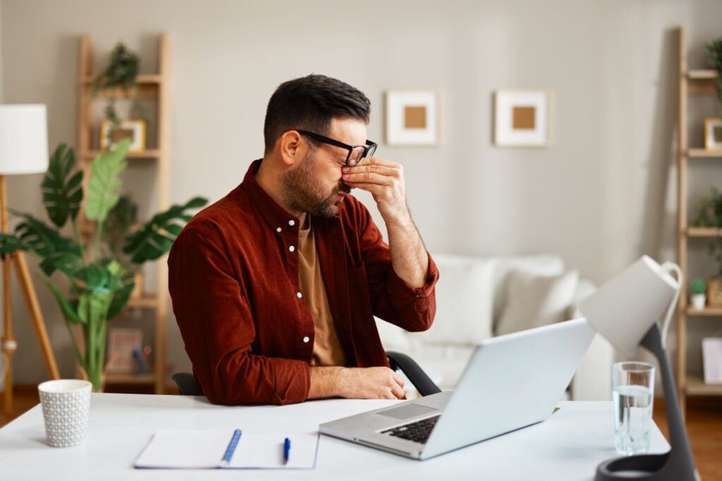 Man rubbing his dry eyes from strain while working on the computer.